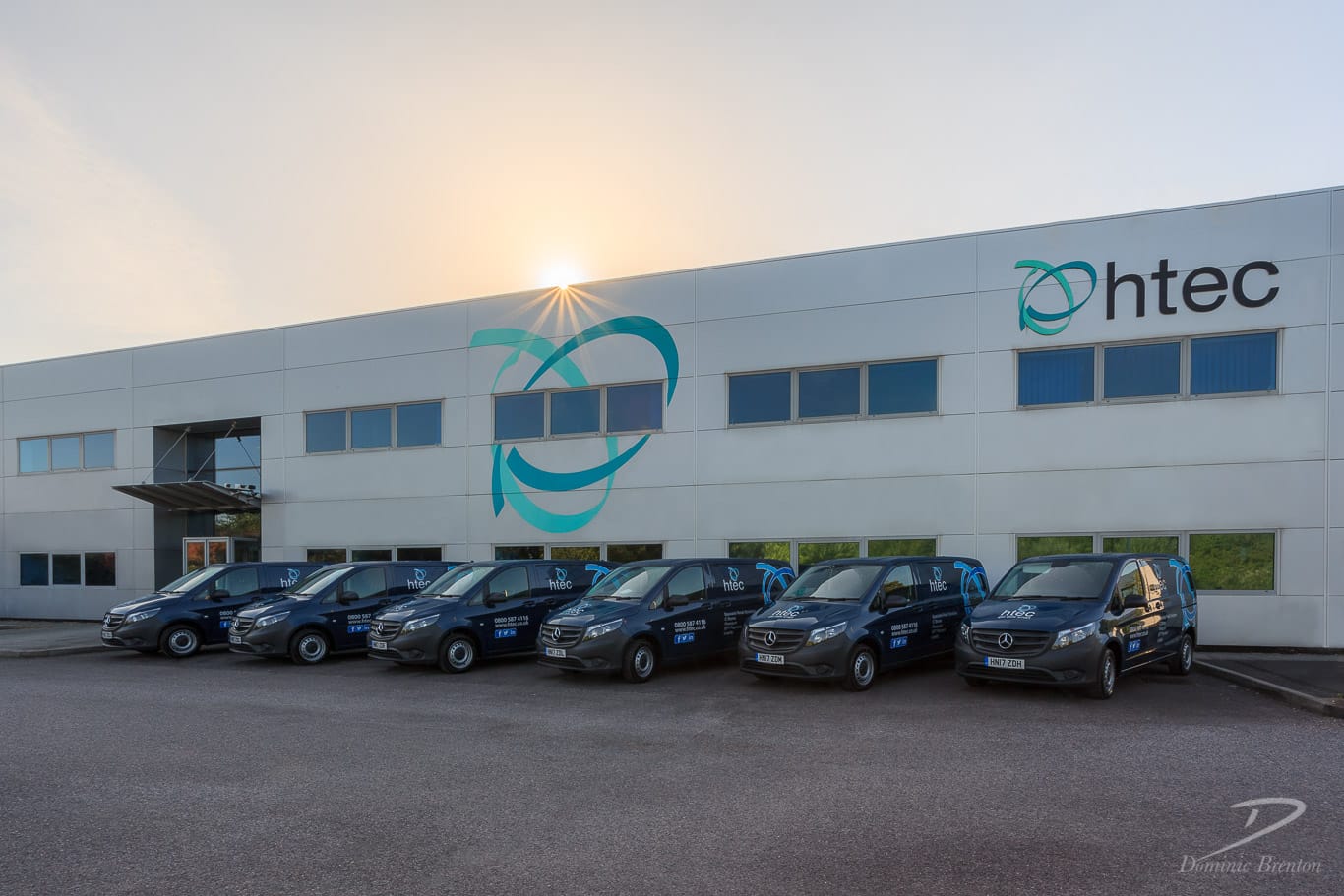 Automated energy management - A modern office building with tan brick and glass windows features a central courtyard. A faint double rainbow appears in the sky above the building. Automated energy management - A modern office building with tan brick and glass windows features a central courtyard. A faint double rainbow appears in the sky above the building.