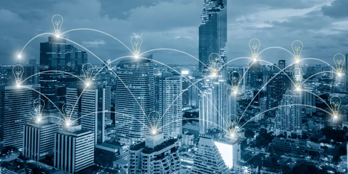 Automated energy management - Two people sit at a desk with a laptop, model wind turbine, hard hat, and solar panel, holding a clipboard displaying an energy efficiency chart with coloured ratings from A to G.