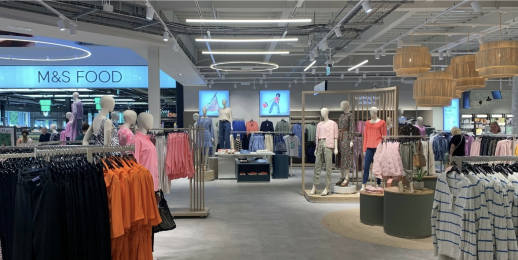 Automated energy management - A well-lit clothes shop interior features mannequins displaying women's outfits, rails of colourful clothes, and a section for food in the background labelled M&S Food. Modern lighting and decor are visible overhead. Automated energy management - A well-lit clothes shop interior features mannequins displaying women's outfits, rails of colourful clothes, and a section for food in the background labelled M&S Food. Modern lighting and decor are visible overhead.
