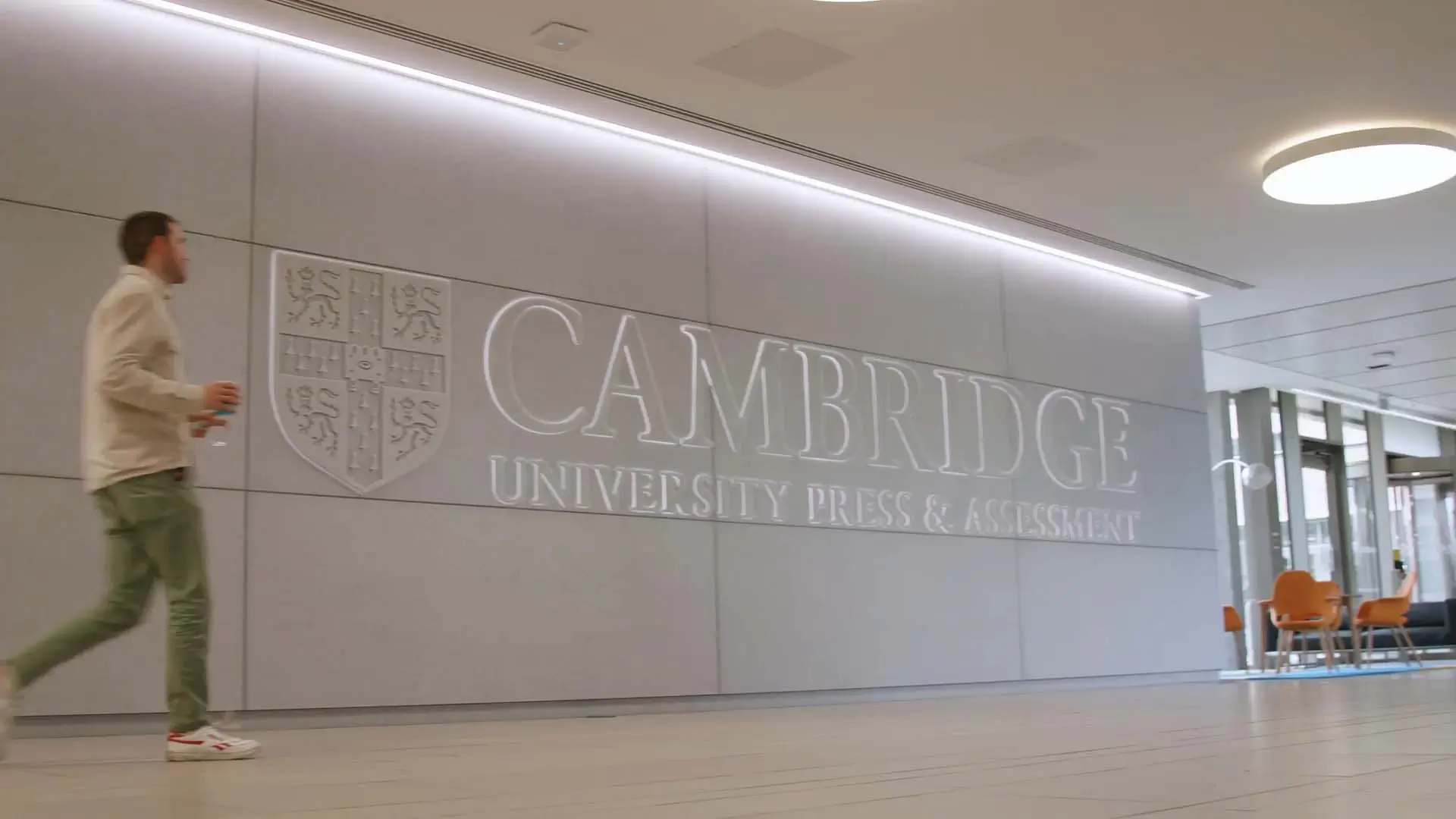 Automated energy management - A person walks past a large wall with the Cambridge University Press & Assessment logo and crest in a modern, brightly lit lobby area. Automated energy management - A person walks past a large wall with the Cambridge University Press & Assessment logo and crest in a modern, brightly lit lobby area.