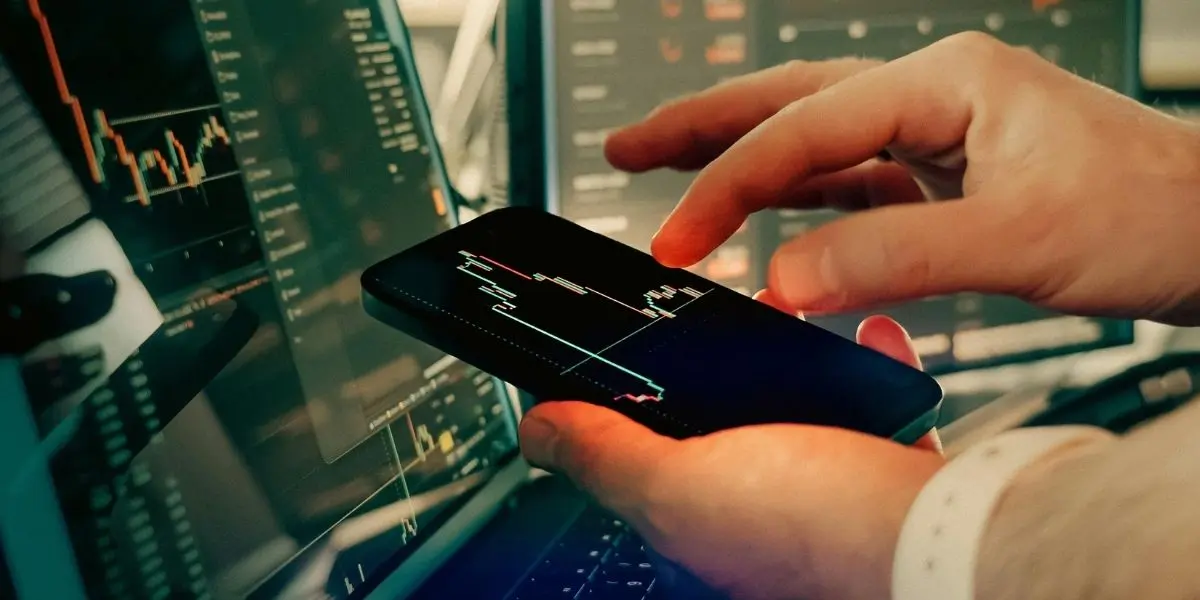 Automated energy management - Two people sit at a desk with a laptop, model wind turbine, hard hat, and solar panel, holding a clipboard displaying an energy efficiency chart with coloured ratings from A to G.