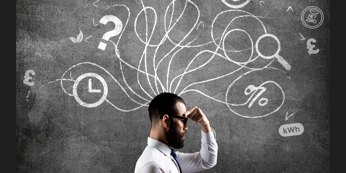 Automated energy management - Two people sit at a desk with a laptop, model wind turbine, hard hat, and solar panel, holding a clipboard displaying an energy efficiency chart with coloured ratings from A to G.