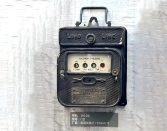 Automated energy management - A vintage black mechanical electricity meter with a rectangular display showing amp, kWh, and voltage, mounted on a wall with a label below indicating manufacturing details.